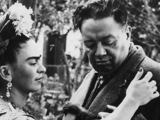 Frida Kahlo y Diego Rivera, una pareja icónica, comparten un momento íntimo. Frida, con flores en el cabello, mira a Diego, quien parece reflexivo.