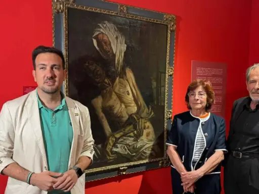 Baldomero Romero Ressendi, junto a dos personas, posa ante un cuadro de temática religiosa en una sala de museo.