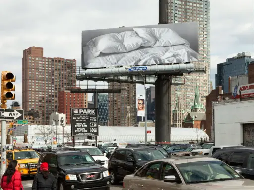 Un cartel de Felix Gonzalez Torres con sábanas arrugadas preside una calle de Nueva York, rodeado de tráfico y edificios.
