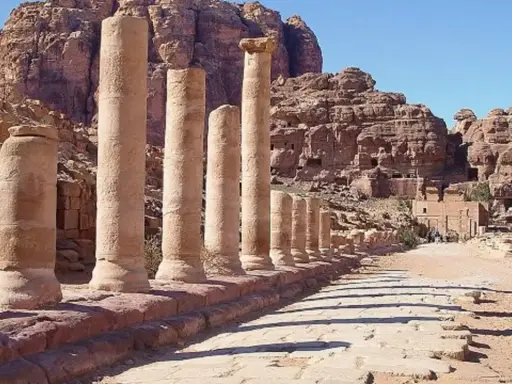 Columnas antiguas en Petra, una de las 7 maravillas del mundo, flanquean un camino de piedra bajo un cielo azul.