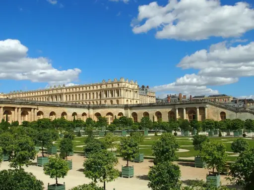 Jardines del Palacio de Versalles, un lugar lleno de curiosidades, con árboles en macetas y un cielo azul con nubes.