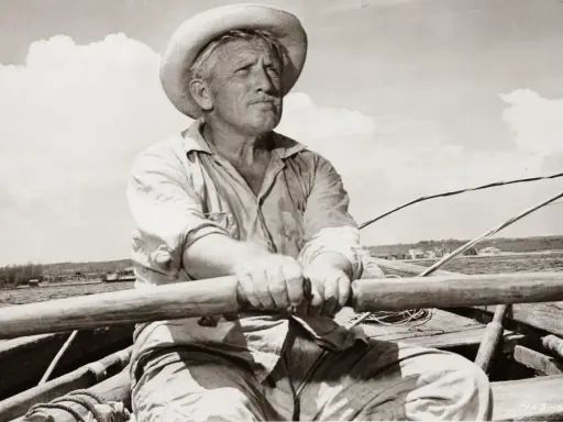Un viejo pescador con sombrero de paja rema en su bote, evocando el espíritu de "el viejo y el mar resumen".