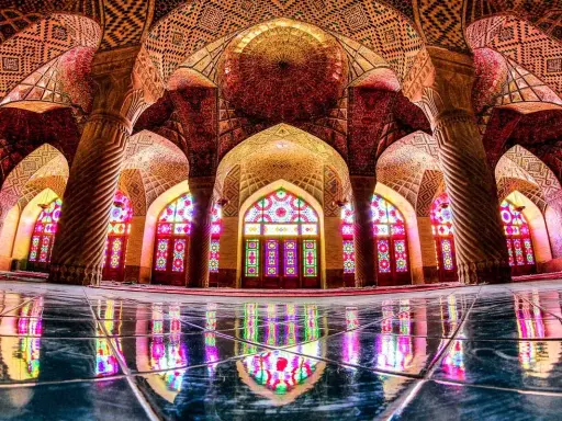 Interior de la mezquita Nasir ol Molk, con arcos intrincados, columnas retorcidas y vitrales de colores que proyectan un caleidoscopio de luz sobre el suelo pulido.