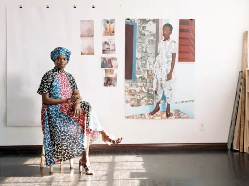 Njideka Akunyili Crosby, sentada en un taburete, luce un vestido vibrante y un turbante. Detrás, obras de arte y fotos familiares adornan la pared.