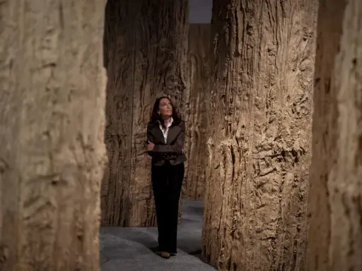 Cristina Iglesias, rodeada de imponentes estructuras de madera que evocan un bosque, contempla la obra.