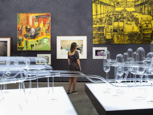 Una curadora de arte observa una instalación de vidrio y pinturas abstractas en una galería.
