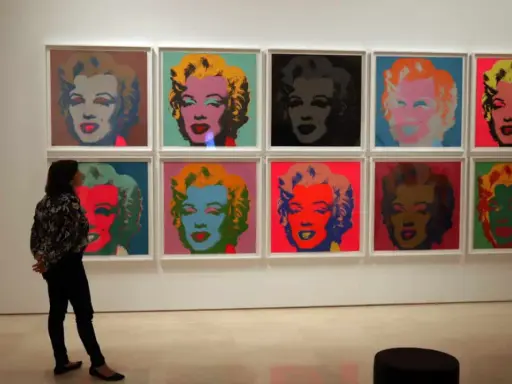 Una persona observa la icónica serie de Marilyn de Andy Warhol, con retratos vibrantes en colores pop.