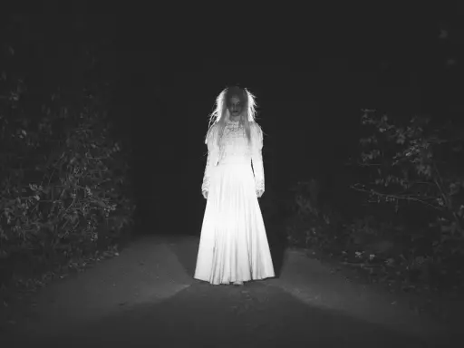 Una figura espectral con un vestido blanco aparece en un camino oscuro, perfecta para cuentos de terror cortos.
