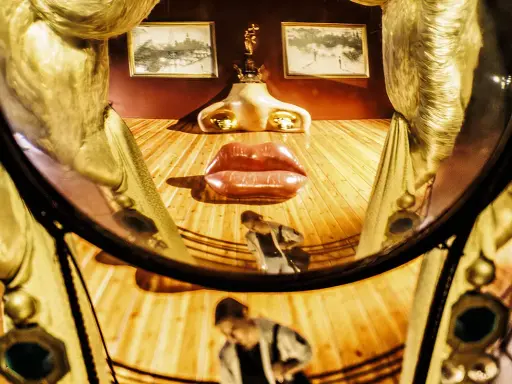 El rostro de Mae West de Dalí, con labios rojos y nariz dorada, se refleja en un espejo curvo.