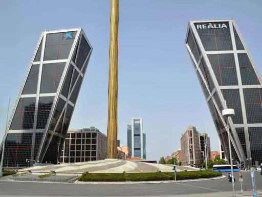 Dos icónicas estructuras diseñadas por Santiago Calatrava se alzan inclinadas, flanqueando una columna dorada.