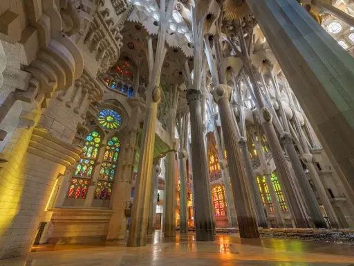 Interior de la Sagrada Familia, una de las **obras de Antoni Gaudí**, con columnas que parecen árboles y vitrales de colores que inundan el espacio.