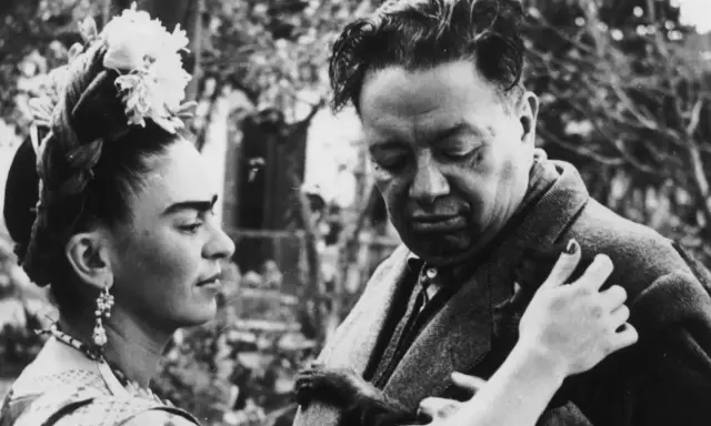 Frida Kahlo y Diego Rivera, una pareja icónica, comparten un momento íntimo. Frida, con flores en el cabello, mira a Diego, quien parece reflexivo.