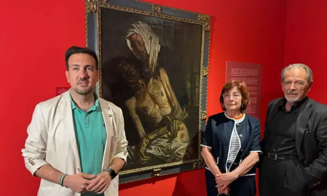 Baldomero Romero Ressendi, junto a dos personas, posa ante un cuadro de temática religiosa en una sala de museo.