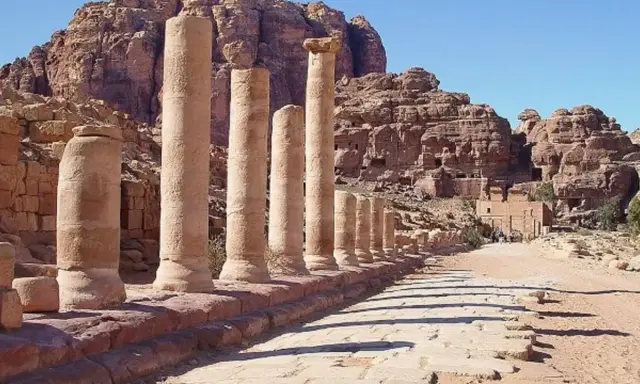 Columnas antiguas en Petra, una de las 7 maravillas del mundo, flanquean un camino de piedra bajo un cielo azul.