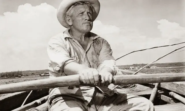 Un viejo pescador con sombrero de paja rema en su bote, evocando el espíritu de "el viejo y el mar resumen".