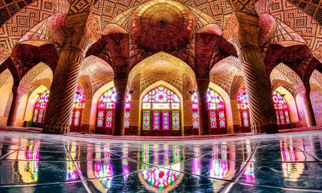 Interior de la mezquita Nasir ol Molk, con arcos intrincados, columnas retorcidas y vitrales de colores que proyectan un caleidoscopio de luz sobre el suelo pulido.