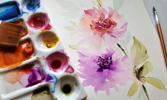 Paleta de acuarelas con pincel y flores en proceso. Inspiración para pintar con acuarelas.