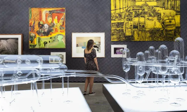 Una curadora de arte observa una instalación de vidrio y pinturas abstractas en una galería.