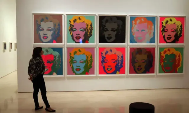 Una persona observa la icónica serie de Marilyn de Andy Warhol, con retratos vibrantes en colores pop.