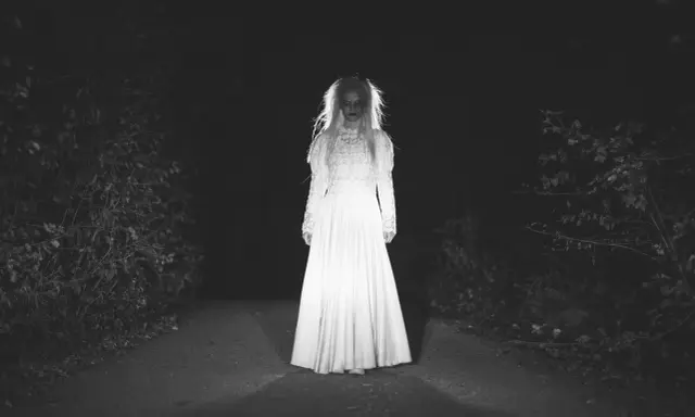 Una figura espectral con un vestido blanco aparece en un camino oscuro, perfecta para cuentos de terror cortos.