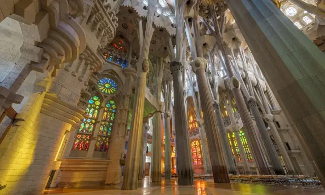 Interior de la Sagrada Familia, una de las **obras de Antoni Gaudí**, con columnas que parecen árboles y vitrales de colores que inundan el espacio.