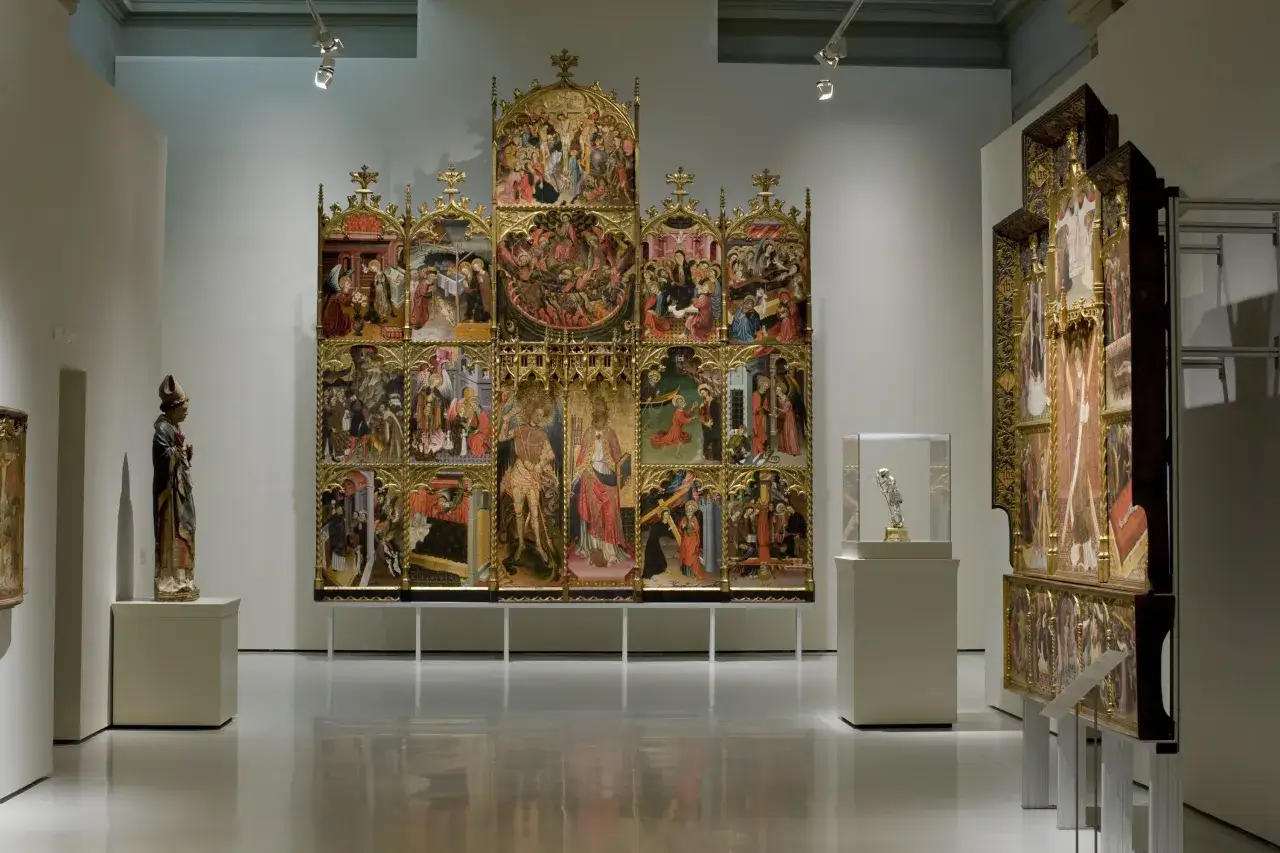 Un retablo g&oacute;tico con escenas religiosas, una pintura al temple detallada, se exhibe junto a una escultura y vitrinas.