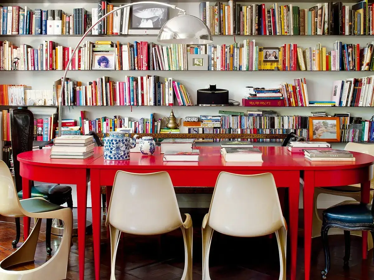 Estanterías llenas de libros recomendados, una mesa roja y sillas modernas crean un espacio acogedor para leer y compartir.