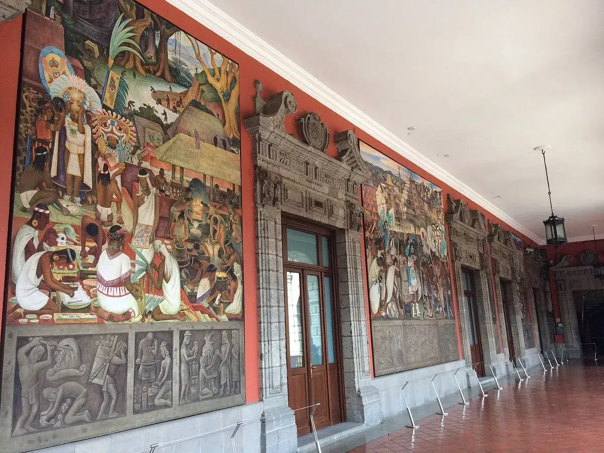 Diego Rivera murales narran la historia prehispánica en un pasillo con arquitectura colonial.