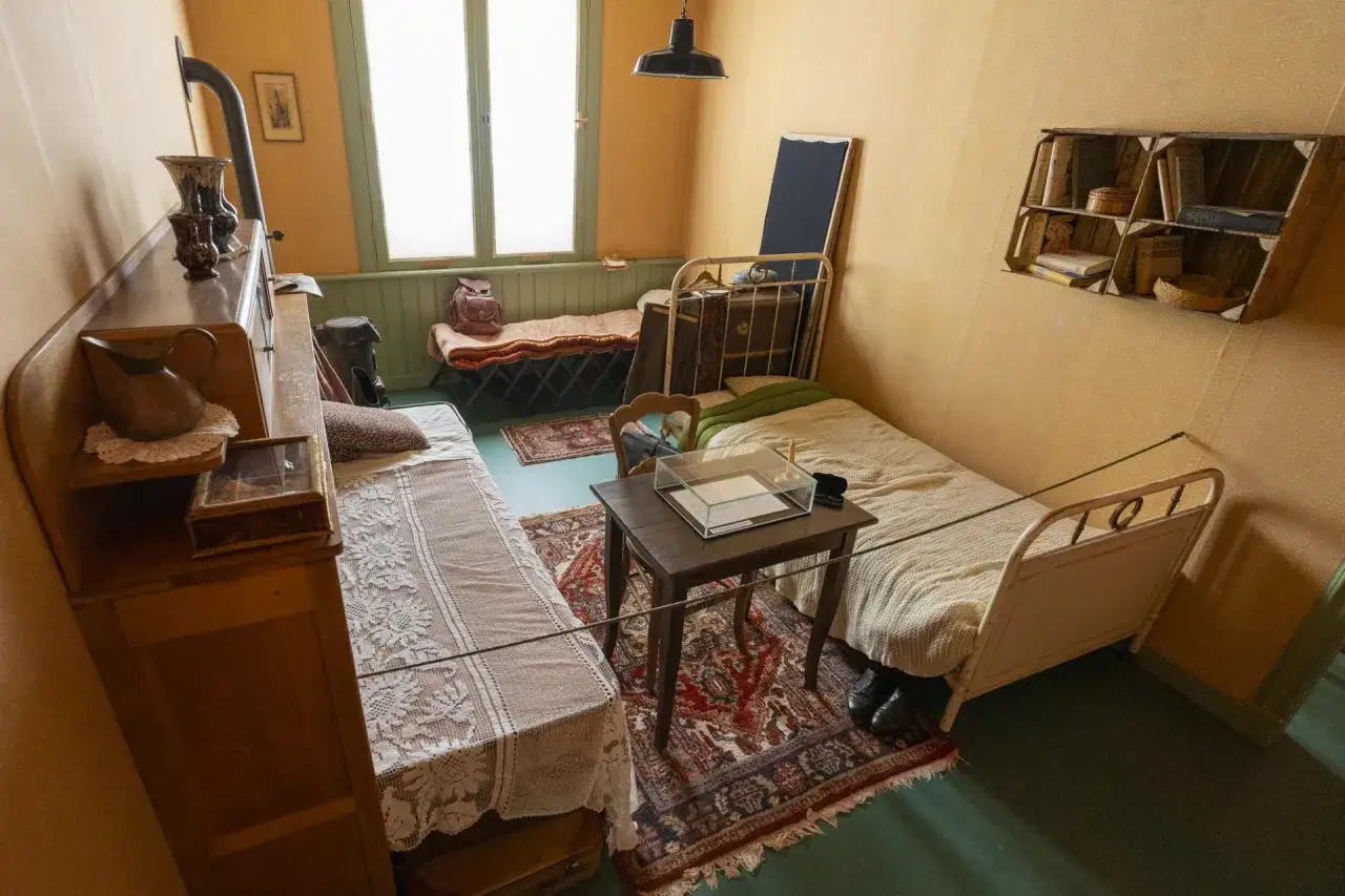 Habitaci&oacute;n sencilla con dos camas, un escritorio y estanter&iacute;as, evocando el ambiente de 