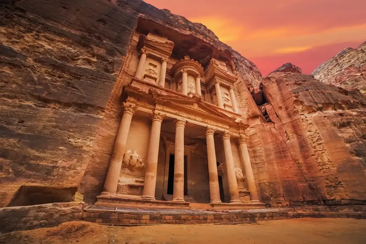 El Tesoro de Petra, una de las 7 maravillas del mundo, emerge de la roca con un cielo anaranjado.