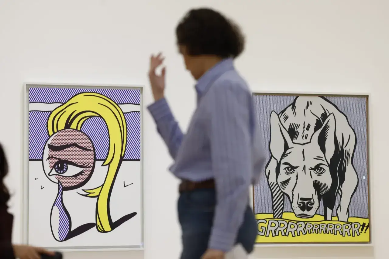 Una persona observa dos obras de arte pop: un primer plano de un ojo lloroso con cabello rubio y un perro gruñendo.