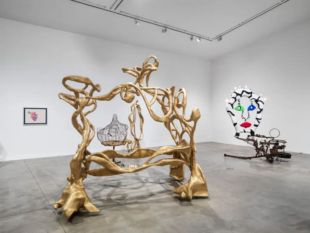 Obras de arte de Niki de Saint Phalle en una galer&iacute;a: una escultura dorada org&aacute;nica, una figura de alambre y una cabeza colorida con luces.