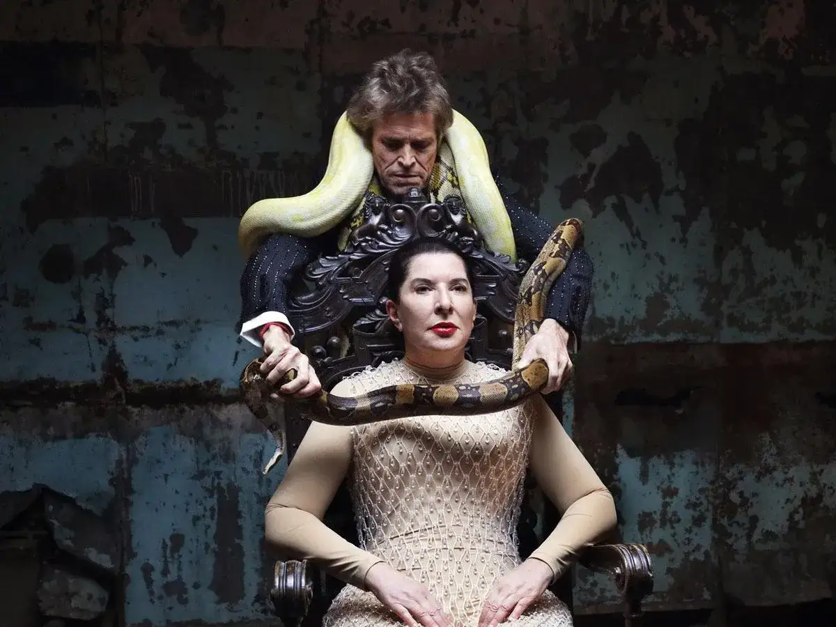 Una mujer sentada con serpientes alrededor, una obra de arte de Marina Abramović que evoca poder y vulnerabilidad.