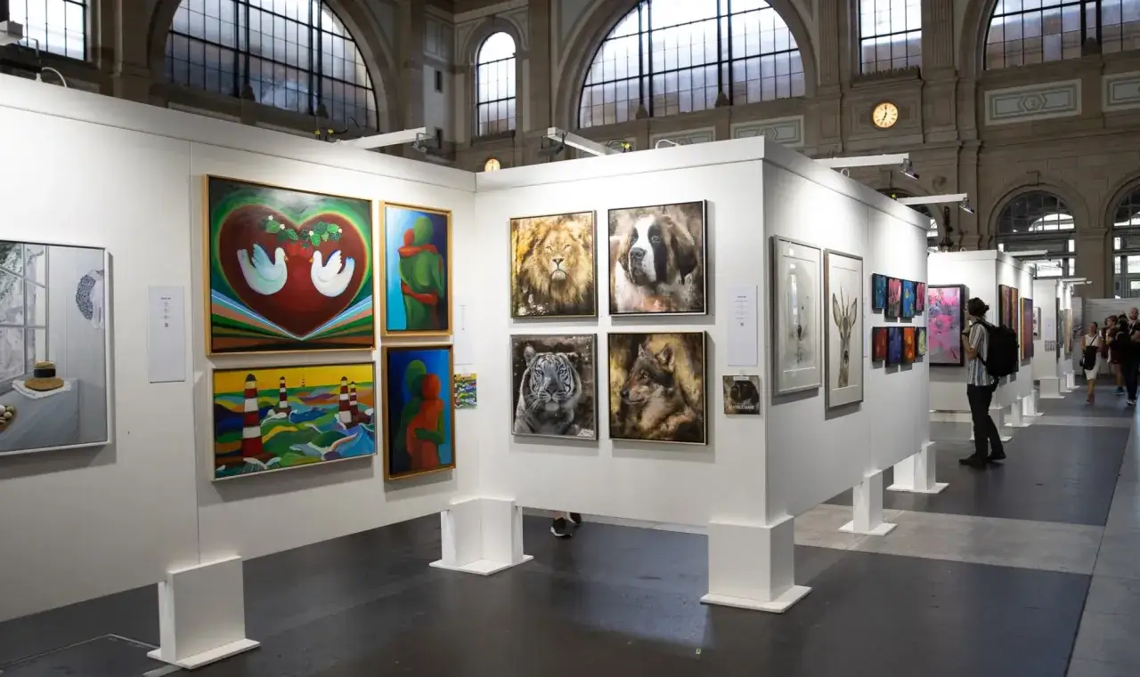 Exhibición de arte con cuadros de animales y paisajes, personas observando las obras en estas ferias de arte.