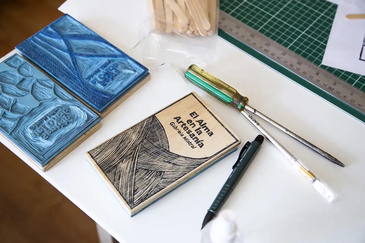Un grabado en arte: sellos de goma, un libro de madera con dise&ntilde;o lineal y herramientas de grabado.