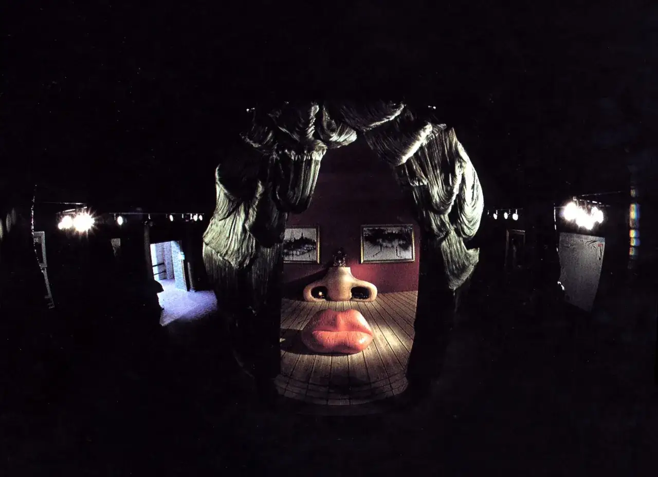 Un rostro surrealista, inspirado en Mae West y el estilo de Dal&iacute;, con labios y nariz prominentes, en un espacio oscuro.
