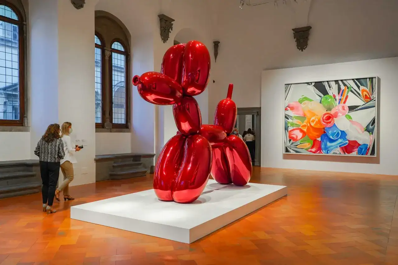 El ic&oacute;nico perro globo rojo de Jeff Koons brilla en una sala de museo, reflejando la luz y el arte circundante.