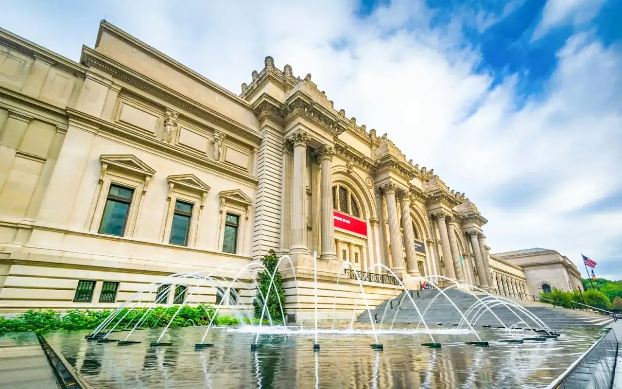 El Museo Metropolitano de Arte de Nueva York, con sus fuentes danzantes y arquitectura imponente, invita a explorar tesoros art&iacute;sticos bajo un cielo azul vibrante.