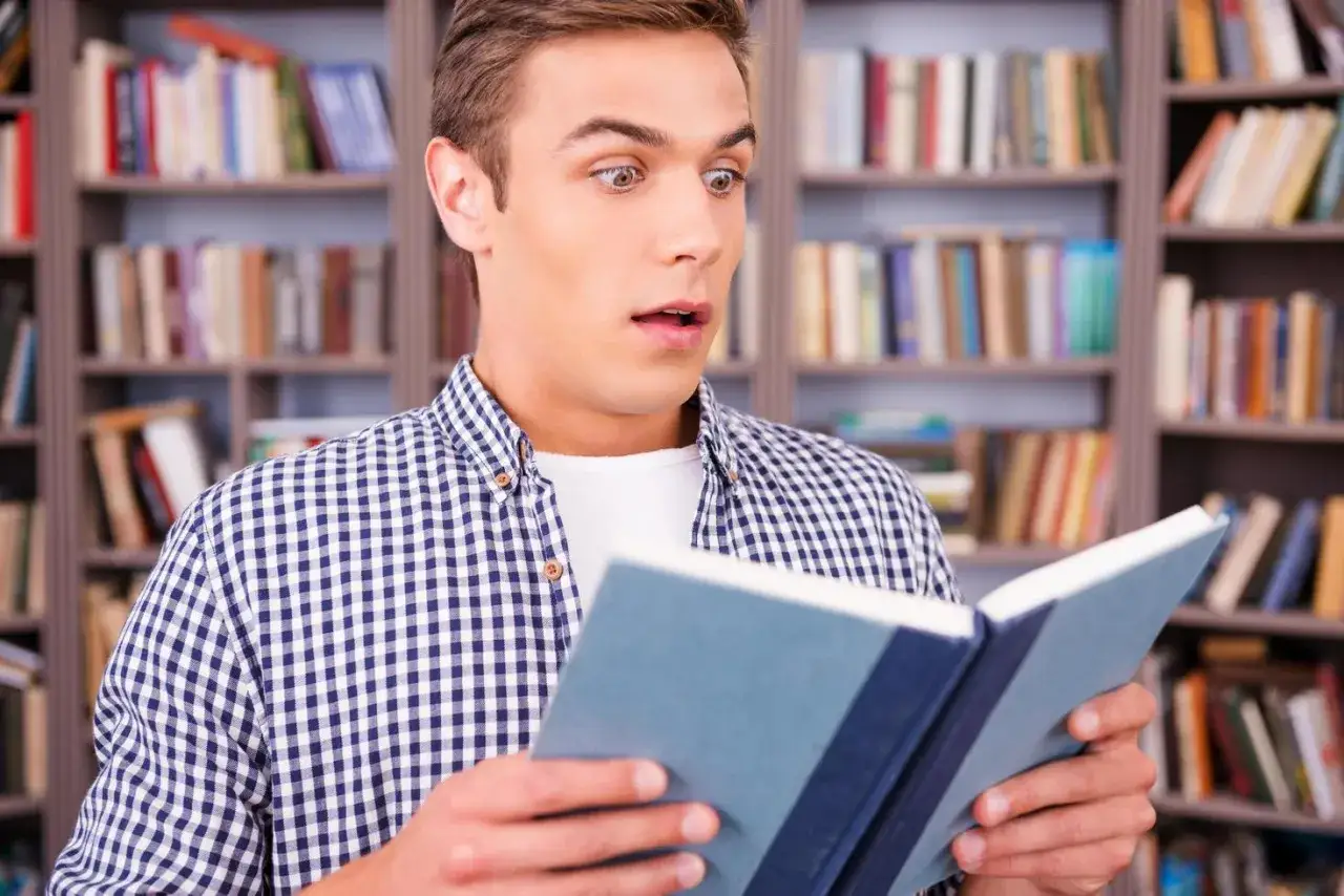 Joven sorprendido leyendo libros para 13 años en una biblioteca.